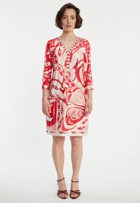 Rood en wit gemusterde jurk met een v-hals en driekwartmouwen, met zwierende bloem- en abstracte ontwerpen. Glad stofoppervlak.