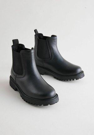 Botas de tobillo negras de cuero con paneles laterales elásticos, suela de goma con taco y lengüetas. Textura suave con un diseño de punta redonda.
