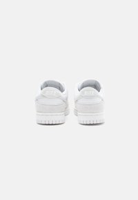 Baltās Nike kedas ar gludu virsu un zamša akcentiem, mīkstinātu apkakli un teksturētu gumijas zoli. "Nike" logotips iespiests uz papēža.
