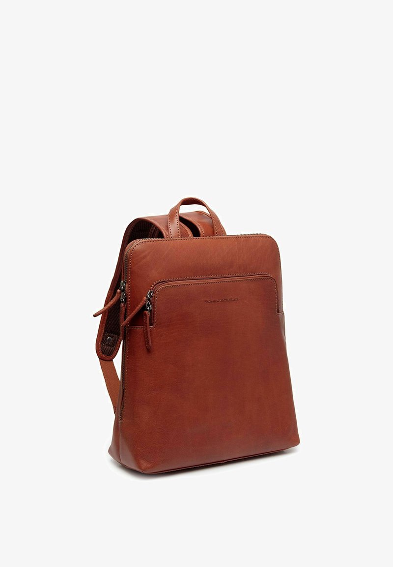 Sac à dos en cuir marron au design simple, comprenant un compartiment principal, une poche zippée à l'avant et deux poignées supérieures pour un transport facile.