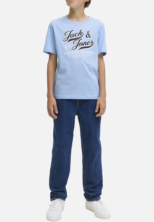 Camiseta de algodón azul claro con texto gráfico en blanco y negro "Jack & Jones". Combinada con vaqueros de denim azul y zapatillas blancas.