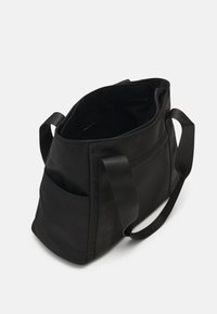 Sac en tissu noir avec une fermeture éclair en haut, de larges bretelles et une poche extérieure. Il présente une texture lisse et un design minimaliste.