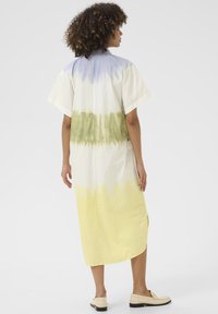 Trumpas rankovėmis, iki kelių ilgio suknelė iš lengvos medžiagos pasižymi mėlynos, žalios ir geltonos spalvų gradientu. Šoninės skeltės pagerina judėjimą.