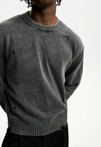 Szary sweter z dzianiny z okrągłym dekoltem, przetarciami, ściągaczami na mankietach i dole oraz fakturowanym wykończeniem.