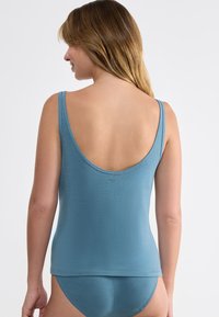 Blaues Tanktop mit dünnen Trägern, weit ausgeschnittenem Rücken und taillierter Passform. Glatte Textur und minimalistischer Stil. Sichtbare passende blaue Panties.