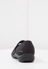 Zapatos negros sin cordones con un upper de tejido texturizado, tira elástica para un ajuste seguro y una suela de goma con un dibujo en relieve.