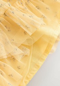 Geltonas tiulio audinys su sluoksniuotais volanais ir subtiliais gėlių raštais. Tekstūra minkšta, lengva ir permatoma.