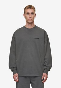 Gray long-sleeve sweatshirt with a round neckline, featuring a small black logo on the chest. Material appears soft with a relaxed fit.