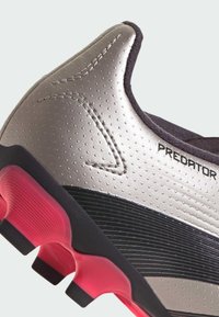 Botín de fútbol Predator con un upper plateado metálico, con puntos texturizados, detalles en negro y una suela de goma rosa con tacos prominentes.