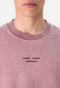 Rosa Sweatshirt mit geripptem Rundhalsausschnitt. Mit schwarzem, gesticktem Text "SAMSØE SAMSØE COPENHAGEN" auf der Brust. Glatte Stoffstruktur.