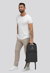 Zaino nero con manico e spallacci regolabili, dotato di una tasca frontale con zip e logo. Realizzato in materiale resistente, design rettangolare.
