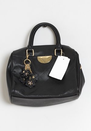 Bolso negro texturizado con doble asa, detalle metálico dorado, llavero floral negro y etiqueta de precio blanca sobre fondo blanco.