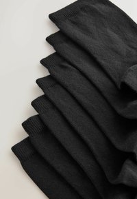 Sept paires de chaussettes noires courtes soigneusement empilées, montrant la texture et les détails des bords-côtes sur un fond clair.
