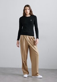 Black knitted sweater with cable pattern, beige pleated trousers, and white sneakers. Simple, fitted top with ribbed cuffs. Minimalist design.