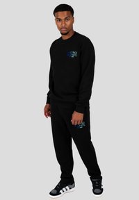 Conjunto de sudadera y pantalones negros de algodón, que presenta un pequeño logo multicolor "WRONG FRIENDS" en el pecho y el muslo.
