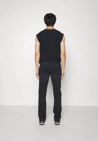 Top senza maniche nero e jeans scuri, con una vestibilità rilassata. Il tessuto ha una texture morbida, con dettagli minimi e senza motivi.