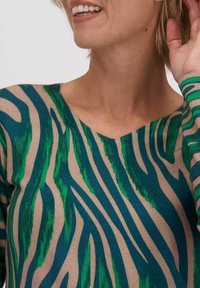 De trui heeft een V-halslijn met een groen en donkerblauw gestreept zebrapatroon op een beige achtergrond. Gemaakt van een gestructureerde gebreide stof.