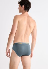 Herren grau Slips mit elastischem Bund, der mit dem gelben "sloggi"-Logo versehen ist. Glattes, dehnbares Material, figurschnittige Passform und sichtbare Nahtdetails.