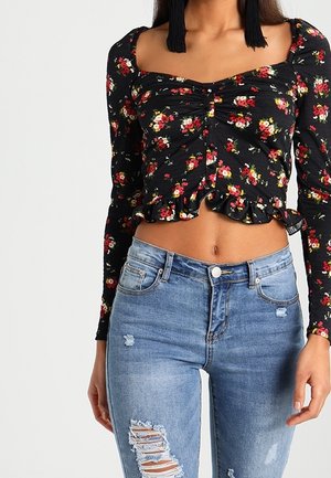 Schwarzes blumiges kurz geschnittenes Oberteil mit langen Ärmeln, gerüschtem Saum und Raffung vorne, kombiniert mit hellblauen, verwaschenen Skinny-Jeans.