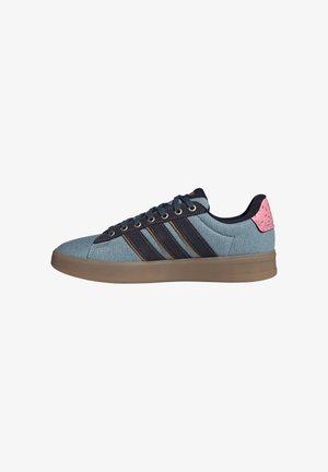 Niedrig geschnittener Sneaker mit blauem Denim-Obermaterial, schwarzen Streifen, brauner Sohle, blauen Schnürsenkeln und pinkfarbenem Fersenlasche mit buntem Streuselmuster.