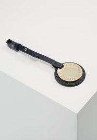 Marineblauer Leder-Kofferanhänger mit einem strukturierten Riemen und einer goldfarbenen, runden Metallplatte, die am Rand mit "EMPORIO ARMANI" geprägt ist.