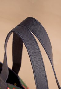 Tummanharmaat kangashihnat, joissa on teksturoitu pinta ja vahvistetut ompeleet kestävyyttä varten, kiinnitetty värikkääseen kangaskassiin.