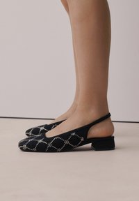 Sorte slingback sko med tekstureret stof, udsmykket med sølvfarvede rhinsten i et diamantmønster, og en lav firkantet hæl.