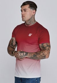 Camiseta de manga corta con degradado rojo, que va de un rojo oscuro a blanco, con un pequeño logotipo blanco en el pecho y una textura suave.
