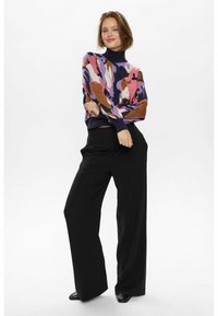 Kelių spalvų megztinis su aukštu kaklu, kurio atspalviai yra rožiniai, violetiniai ir rudi. Suderintas su juodomis plačiomis kelnėmis ir juodais batais.