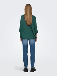 Vihreä, löysä neulepaita, jossa on lepakkohihat, yhdistettynä slim fit -sinisiin farkkuihin ja mustiin kenkiin. Pehmeä tuntuma, monivärinen ulkonäkö.