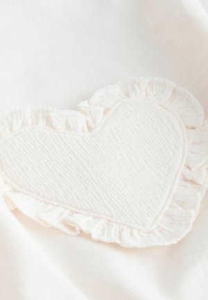 Heleroosa kangas, millel on südamekujuline plaat tekstuurse pinnaga ja triibuliste äärtega, ühtlase valge tausta taustal.