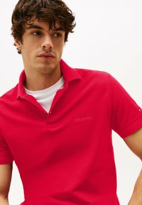 Rode polo shirt met een gestructureerde stof, korte mouwen en een prominent kraag. Kenmerkt een geborduurd "HILFIGER" logo op de linkerkant van de borst.