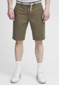 Olivgrüne Shorts aus Baumwolle, ausgestattet mit einem weiß-braun gewobenen Gürtel, Seitentaschen und einem geraden Schnitt, der oberhalb des Knies endet.