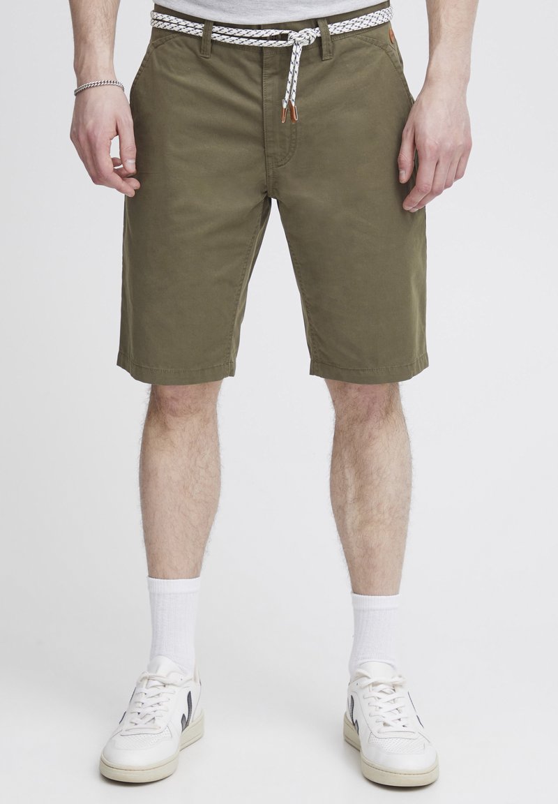 Olivgrüne Shorts aus Baumwolle, ausgestattet mit einem weiß-braun gewobenen Gürtel, Seitentaschen und einem geraden Schnitt, der oberhalb des Knies endet.