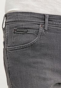 Grå denimjeans har en klassisk design med raka ben, femficksstil, detaljerad sömnad och en något sliten textur.