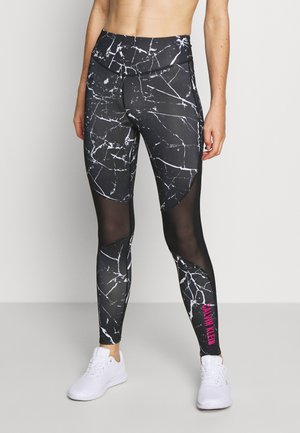 Leggings con patrón de mármol en blanco y negro, con paneles de malla y el logo rosa de "Calvin Klein" en la parte inferior de la pierna, combinados con zapatillas deportivas blancas.