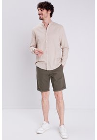 Ljusbeige långärmad skjorta med knapppdetaljer, ihop med olivgröna shorts. Vita sneakers fulländar den avslappnade stilen.