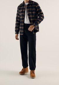 Flanellipaita laivastonsinisen ja oranssin ruutukuvion kanssa, yhdistetty mustiin housuihin ja ruskeisiin nauhallisiin saappaisiin, joissa on sileä pinta ja napin yksityiskohdat.