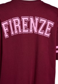 Vínová bavlnená tričko s nápisom "FIRENZE" v tučných ružových písmenách na chrbte, s dvoma bielymi pruhmi na rukávoch.