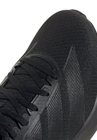 Schwarzer Sportschuh mit einem Obermaterial aus Mesh, strukturierten Akzenten, flachen Schnürsenkeln und einem eleganten, abgerundeten Zehendesign mit einer gepolsterten Sohle.