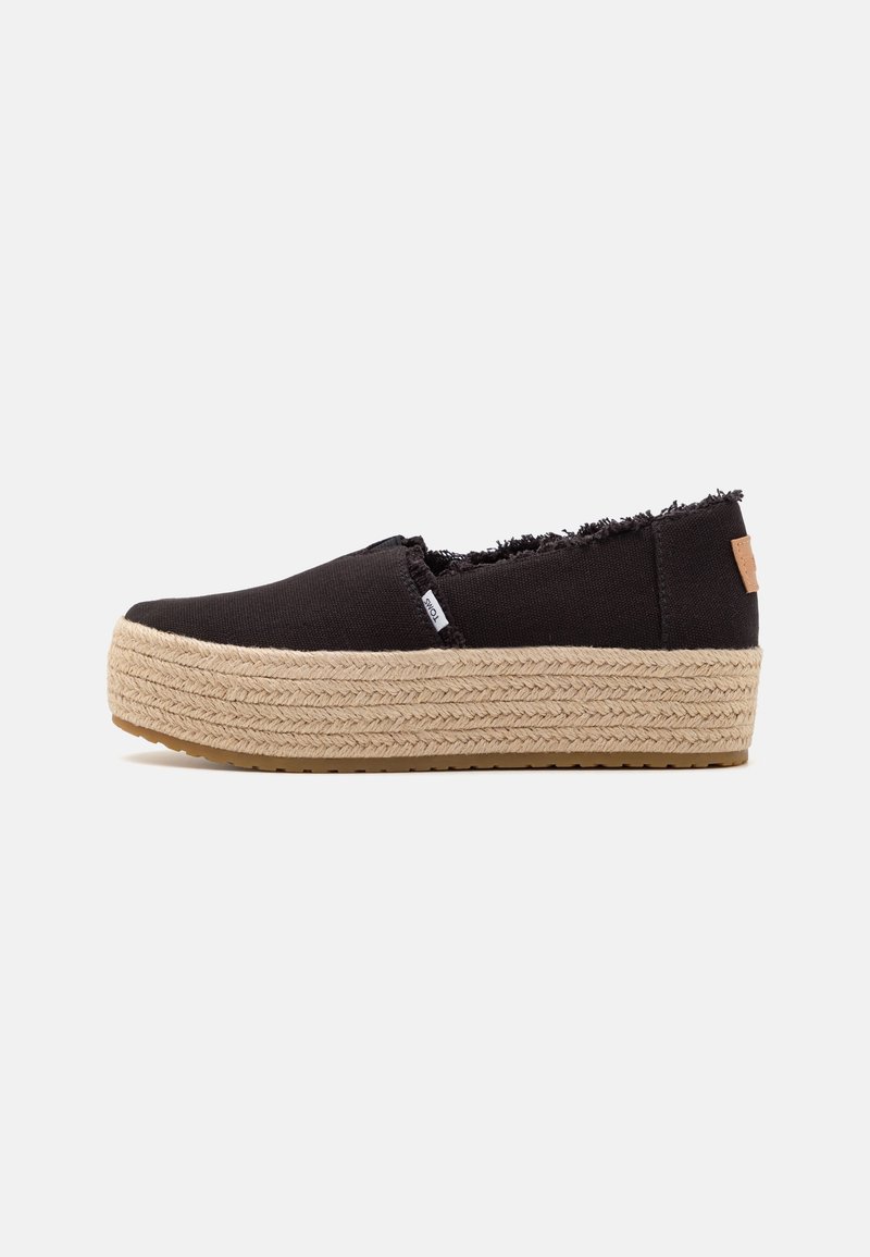Baskets noires à enfiler avec bords effilochés, semelle plateforme épaisse tressée beige, et petite étiquette de marque en tissu sur le côté.