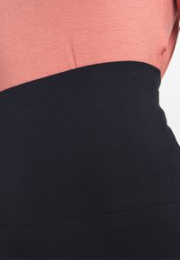 Top bicolore con sezione superiore rosa e sezione inferiore nera, realizzato in tessuto liscio e elastico. Dettaglio della cucitura visibile al passaggio di colore.