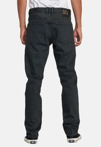 Jeans de corte slim para hombre en denim gris oscuro, con una cinturilla estándar, dos bolsillos traseros y detalle del logo en la cinturilla.