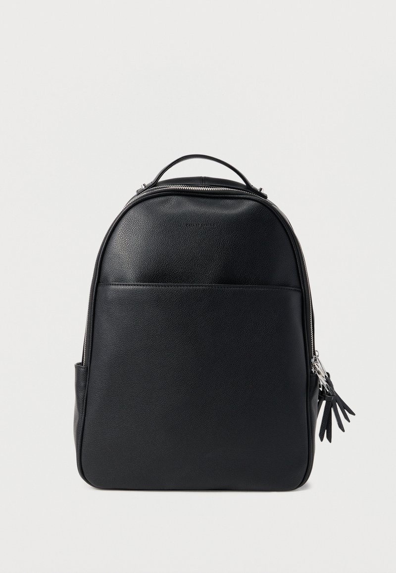 Μαύρο δερμάτινο σακίδιο πλάτης με χειρολαβή στο πάνω μέρος, τσέπη μπροστά και διπλά ασημένια φερμουάρ με δερμάτινες φουντίτσες, απεικονίζεται σε απλό ανοιχτό φόντο.