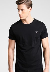 Black short-sleeve t-shirt made of cotton with a crew neck. Features a small embroidered logo on the left chest. Smooth texture.