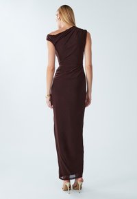 Lange, aansluitende jurk van donkerbruin stof met een ontwerp met één schouder. Gladde textuur en gedrapeerde details verbeteren de silhouet.