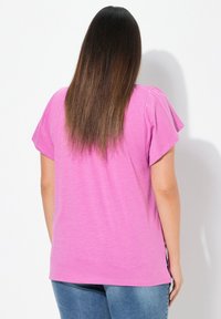 Růžové tričko s krátkým rukávem, volného střihu, z lehkého materiálu, s bočními rozparky, v kombinaci s modrými džíny. Pohled zádové strany zobrazuje rovné vlasy.