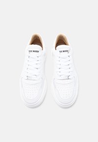 Ζευγάρι λευκά αθλητικά παπούτσια Steve Madden με διάτρητες μύτες, κορδόνια και λογότυπο στη γλώσσα και στην ετικέτα των κορδονιών, που φαίνεται από ψηλά.