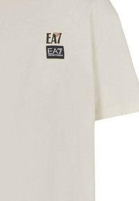 Kermavaaleat lyhythihaiset puuvillat-paidat, joissa on kaksi pientä Emporio Armani EA7 -logoa painettuna vasempaan ylös rintaan.