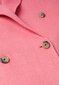 Růžový vlněný kabát s měkkou texturou, s klasickým límcem a třemi hnědými knoflíky s tmavým středem na přední straně.